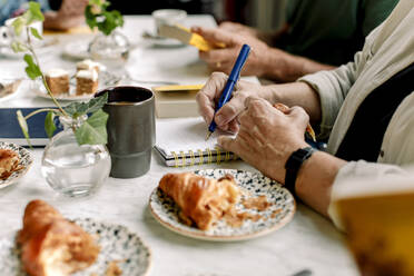 Hände einer älteren Frau, die in einem Café Tagebuch schreibt - MASF33319