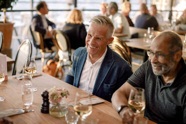 Glücklicher älterer Mann sitzt mit einem männlichen Freund im Restaurant - MASF33331