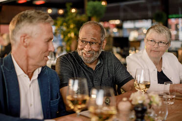 Lächelnder älterer Mann im Gespräch mit einem männlichen Freund, während er neben einer Frau im Restaurant sitzt - MASF33332