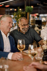 Cheerful male friends with wineglasses enjoying while sitting in restaurant - MASF33333