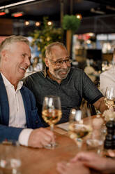 Fröhliche männliche Freunde mit Weingläsern, die in einem Restaurant sitzen und genießen - MASF33333