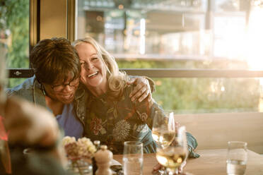 Lächelnde ältere Frau mit Arm um fröhlichen Freund genießt im Restaurant - MASF33334
