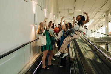 Teenager-Mädchen mit erhobener Hand genießt auf Rolltreppe in Einkaufszentrum - MASF33346