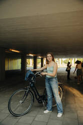 Porträt eines Teenagers mit Fahrrad unter einer Brücke stehend - MASF33370