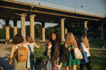 Porträt eines lächelnden Mädchens im Teenageralter, das mit Freunden gegen eine Brücke im Park läuft - MASF33377