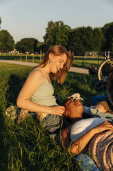 Smiling teenage girl talking with female friend lying on lap at park - MASF33381