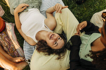 High angle view of smiling teenage girl lying on friend's lap at park - MASF33382