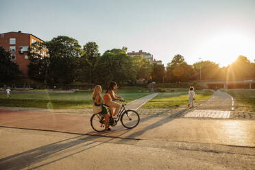 Teenager-Mädchen sitzt mit einem Freund auf dem Fahrrad im Park bei Sonnenuntergang - MASF33387