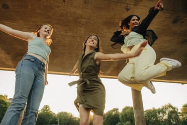 Low angle view of happy teenage girls jumping under bridge - MASF33393