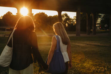 Teenager-Mädchen halten sich an den Händen, während sie im Park bei Sonnenuntergang spazieren gehen - MASF33397
