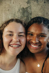 Glückliches Teenager-Mädchen, das eine Zahnspange trägt, mit einer Freundin an der Wand - MASF33400