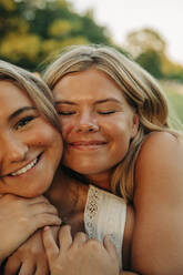 Smiling girl with eyes closed hugging blond female friend - MASF33407