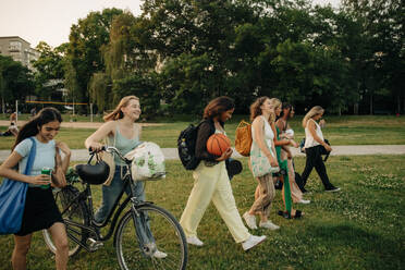 Smiling teenage girls walking together at park during sunset - MASF33425