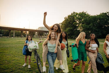 Happy teenage girl giving piggyback ride to female friend at park - MASF33426