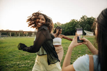 Teenage girl photographing happy female friends dancing in park - MASF33434