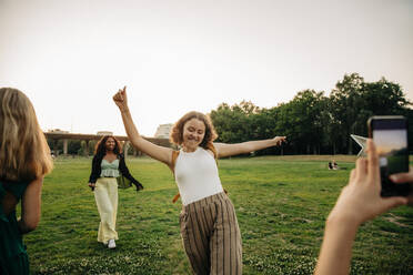 Teenage girl photographing carefree female friend dancing at park during sunset - MASF33436