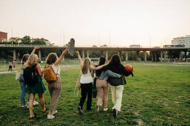 Rückansicht von Teenagermädchen mit erhobener Hand, die von Freunden im Park spazieren gehen - MASF33443