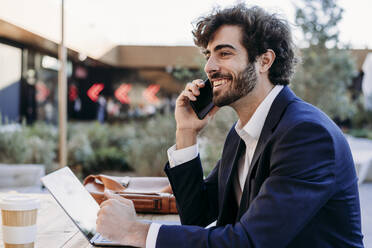 Happy businessman talking on smart phone sitting in cafe - EBBF07037