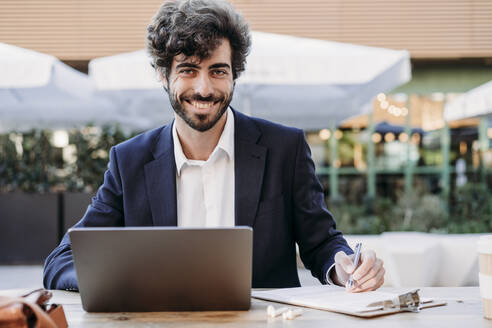 Handsome businessman with document and laptop working in cafe - EBBF07045