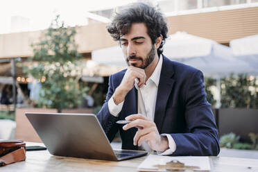 Focused businessman with hand on chin looking at laptop - EBBF07047