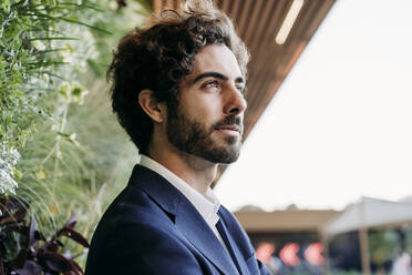 Handsome young businessman day dreaming near plants - EBBF07063