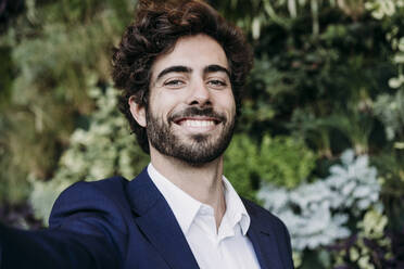 Handsome happy businessman with plants in background - EBBF07067