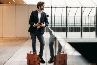 Businessman with smart phone leaning on glass railing - EBBF07069