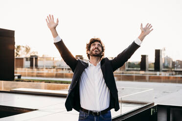 Carefree businessman with arms raised near railing - EBBF07079