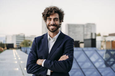 Handsome urban businessman wearing blazer standing with arms crossed - EBBF07094