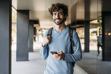 Young handsome man with smart phone standing in corridor - EBBF07109