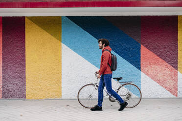 Mann mit Fahrrad auf Fußweg vor bunter Wand fahrend - EBBF07118
