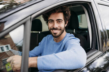 Lächelnder gutaussehender junger Mann, der im Auto reist - EBBF07123