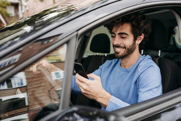 Lächelnder Mann mit Smartphone im Auto sitzend - EBBF07126