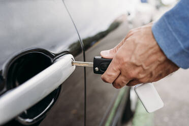 Hand eines Mannes, der ein Auto mit einem Schlüssel abschließt - EBBF07131