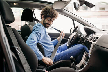 Young man fastening seat belt sitting in car - EBBF07132