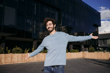 Carefree young man with arms outstretched enjoying in front of building - EBBF07137