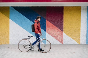 Mann fährt Fahrrad vor einer bunten Wand - EBBF07143