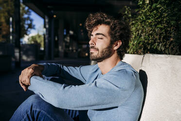 Man enjoying sunlight sitting by wall - EBBF07150