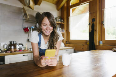 Lächelnde junge Frau benutzt ihr Smartphone in der Küche zu Hause - GIOF15599
