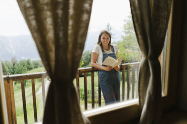 Glückliche junge Frau mit Buch durch Fenster gesehen - GIOF15610
