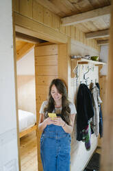 Smiling young woman using smart phone in doorway - GIOF15622