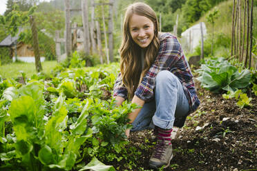 Glückliche junge Frau pflanzt Gemüse im Garten - GIOF15631