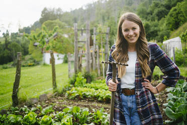 Happy woman standing with rake in vegetable garden - GIOF15632