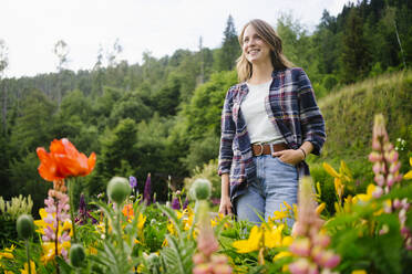 Glückliche junge Frau steht inmitten von Blumen auf einem Feld - GIOF15634