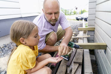 Vater und Tochter bauen hockend vor dem Haus eine Holzwand - KMKF01890
