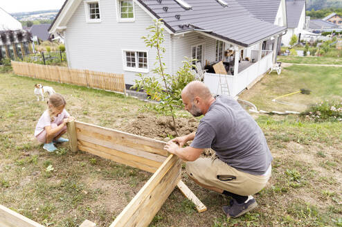 Vater und Tochter machen ein Hochbeet im Hinterhof in der Nähe des Hauses - KMKF01902