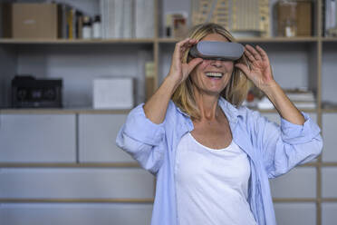 Happy mature woman wearing virtual reality glasses at home - RIBF01211
