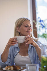 Lächelnde reife Frau hält eine Tasse Kaffee zu Hause - RIBF01216