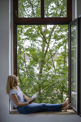 Frau, die zu Hause am Fenster sitzt und ein Buch liest - RIBF01234