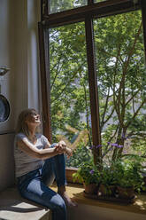 Woman sitting with eyes closed near window at home - RIBF01244